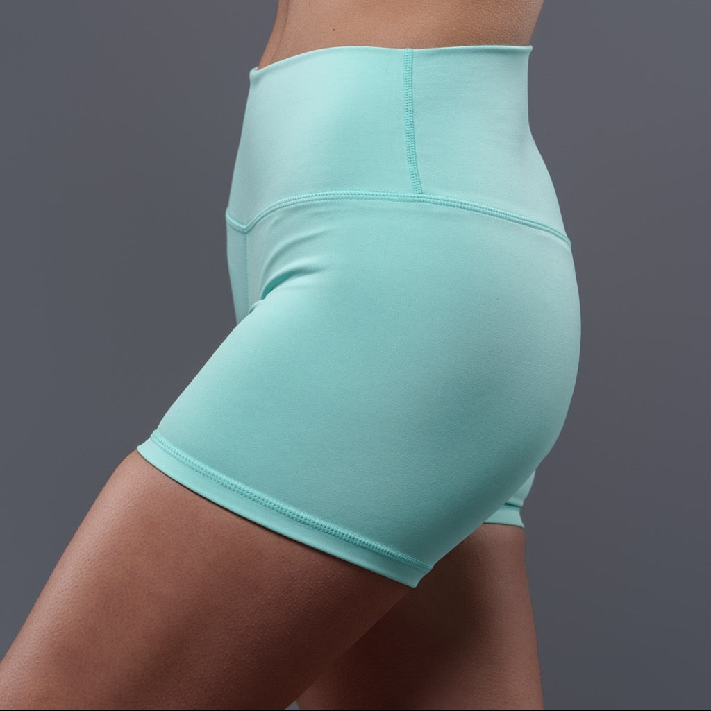 A person wearing Allure Mint Shorts, featuring a sleek fit in light blue, poses against a plain gray background, showing the side and part of the front hip and thigh.