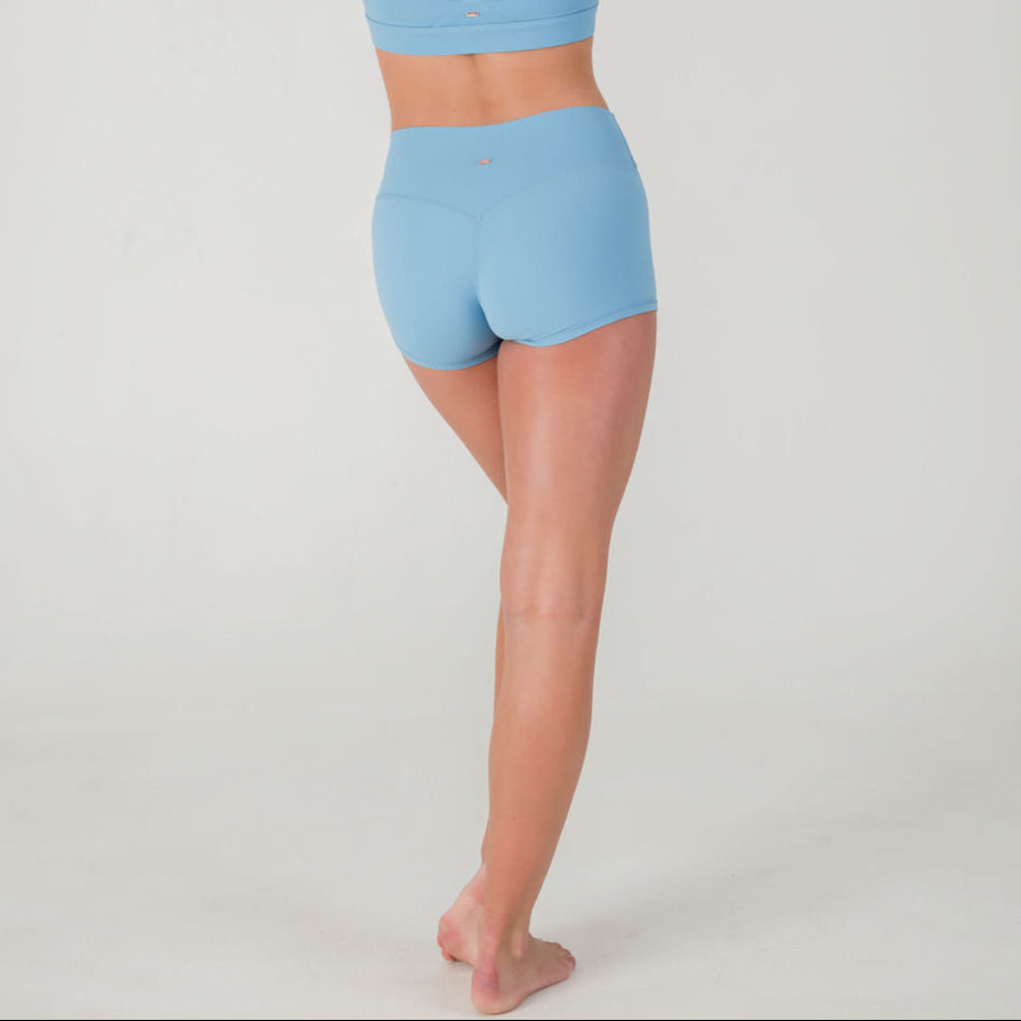 A person stands barefoot on one leg, facing away from the camera, wearing a light blue sports bra and FRESH Shorts - Sky blue, set against a plain white background.