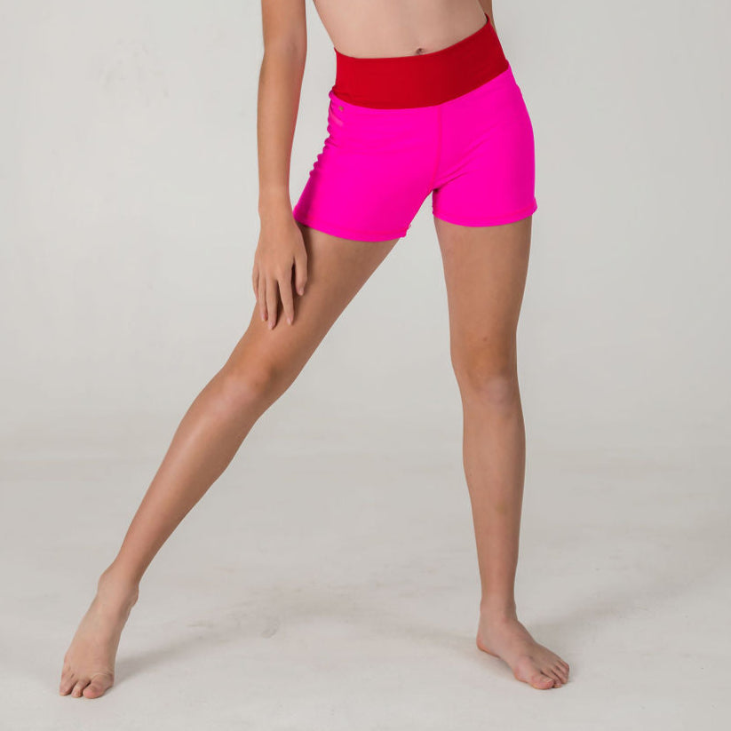 Model poses barefoot against a plain background, showcasing the lower torso and legs in Chic Shorts - Punch Pink (FINAL SALE), featuring bright pink fabric and a bold red waistband.