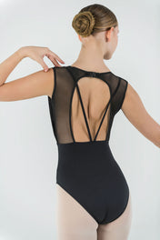 A ballerina with a neat bun showcases the Opera Leotard’s crisscross mesh and sheer back, posing gracefully with one arm raised against a plain backdrop—the perfect statement piece for any dance wardrobe.