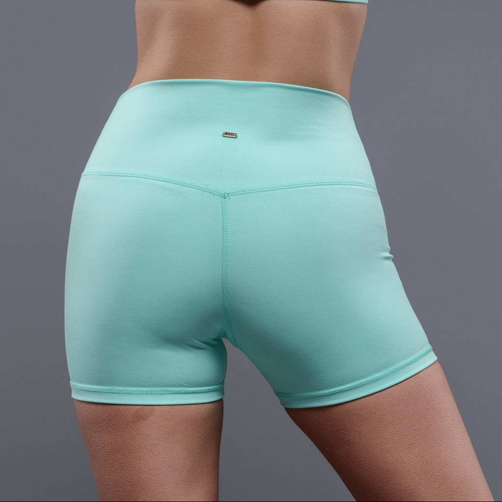 A person models the high-waisted Allure Shorts - Mint, shown from the waist down and from the back against a plain gray background, highlighting their flattering fit.