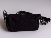 The Crossbody bag is a small black corduroy crossbody with a zip closure and a black-and-white striped adjustable strap, shown on a light gray background.