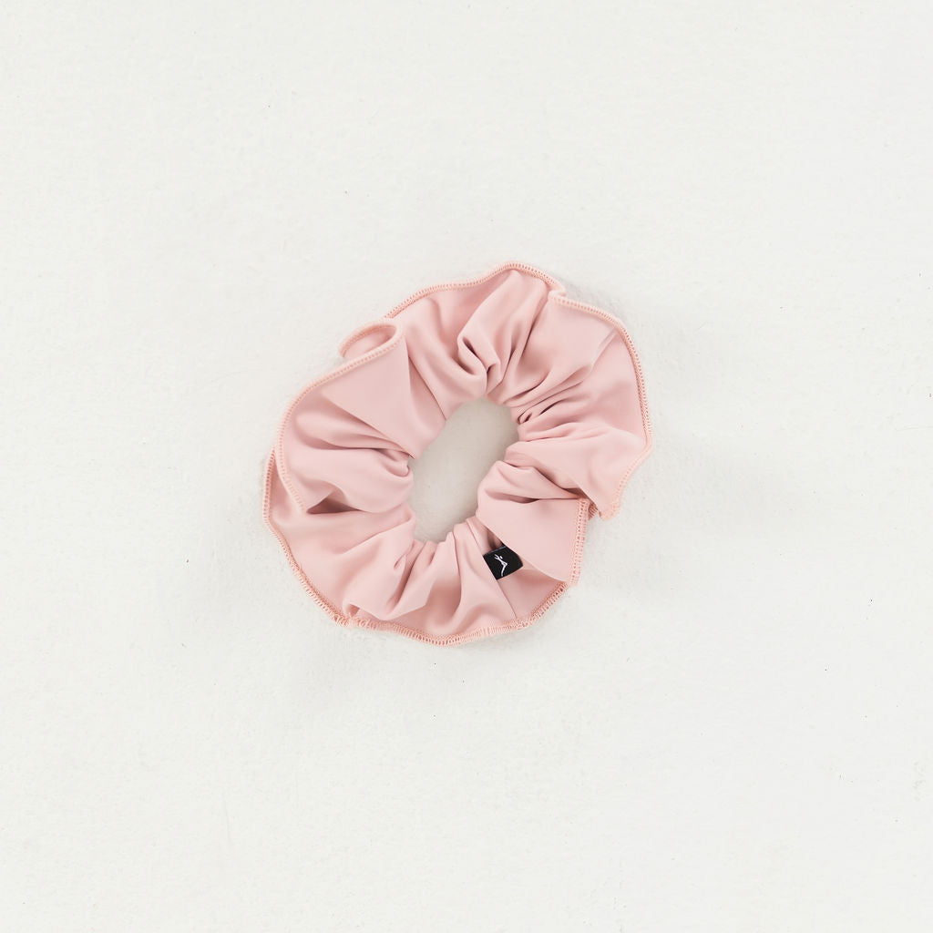 Part of the Scrunchies 2 Pack, this light pink scrunchie with a small black tag adds a stylish touch to your look and is shown on a white background.