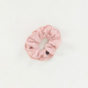 Part of the Scrunchies 2 Pack, this light pink scrunchie with a small black tag adds a stylish touch to your look and is shown on a white background.