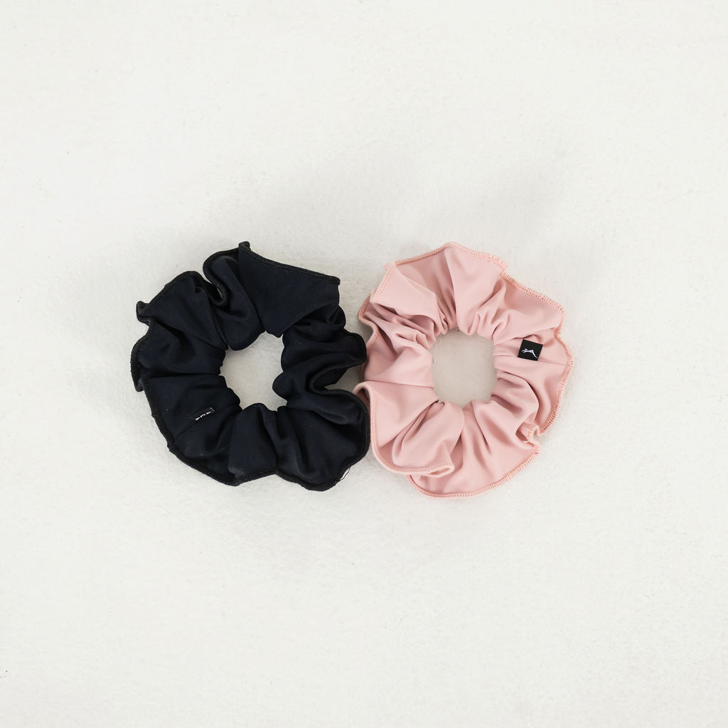 The Scrunchies 2 Pack features a black and a pink fabric scrunchie side by side on a light surface, adding a simple, stylish touch.