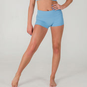A person stands barefoot against a plain background, wearing sky blue FRESH Shorts and a matching sports bra. One leg is slightly bent and their hand rests on their thigh, showcasing the comfortable activewear.