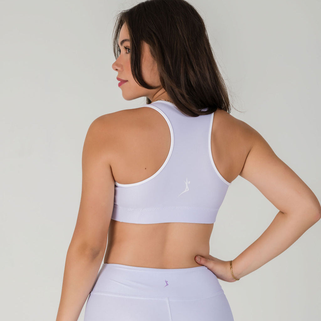 A woman with long brown hair, wearing the Lavender Lux Airsoft Sports Top and matching moisture-wicking shorts, stands with her back to the camera and hand on her hip against a plain light background.