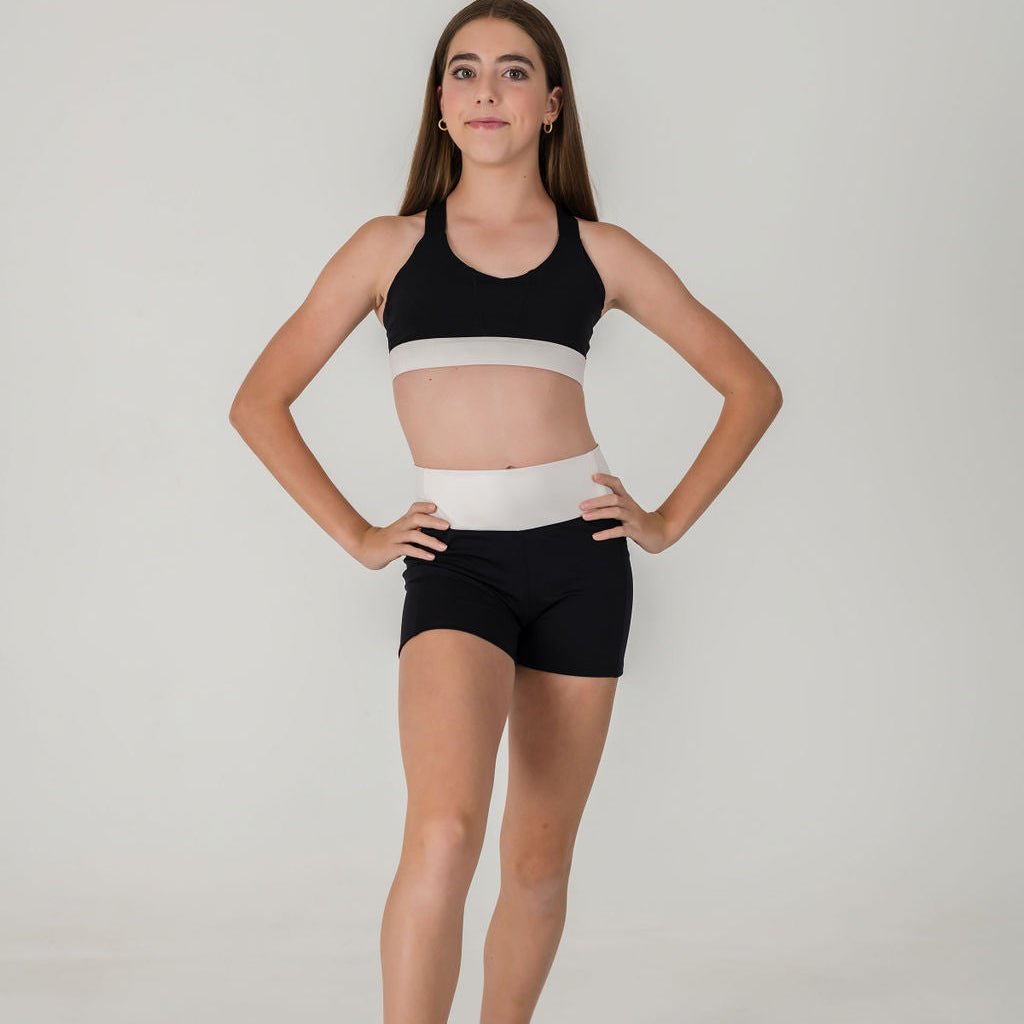 Barefoot model poses in a studio, wearing Chic Shorts - Charcoal and a black and white crop top, hands on hips, cropped from shoulders down against a plain white background.