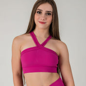 A young woman with long brown hair smiles while wearing the Iconic Top - Pink, a bright ribbed halter, standing against a plain light gray background.
