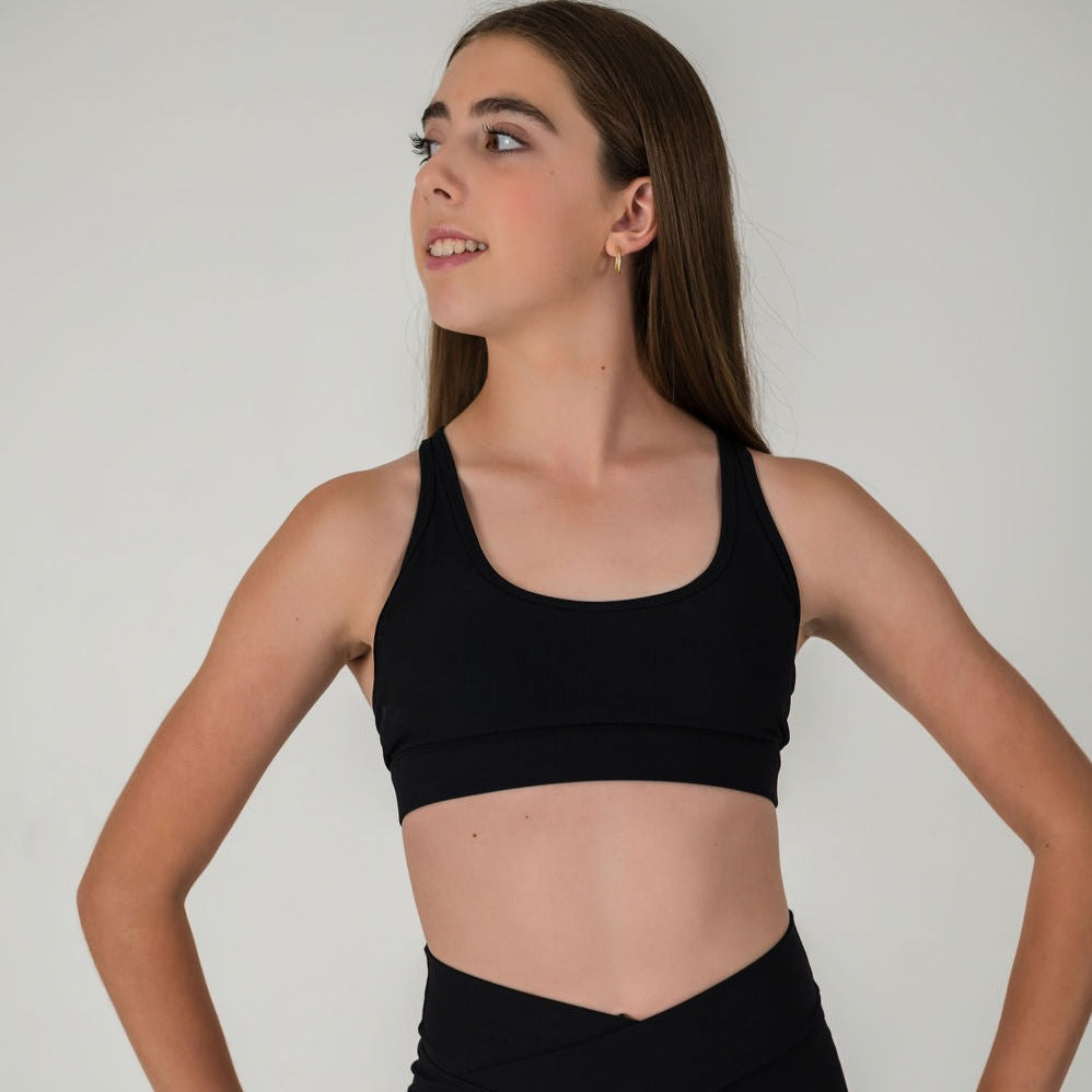 A young girl with long brown hair wears the 2Iconic Sport Bra and matching high-waisted leggings, standing hands on hips and looking to the side against a plain light background, ready for any workout.