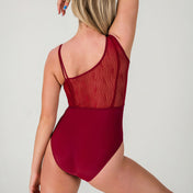 A woman poses with her back to the camera, wearing the Eden Leotard - Wine, which features sheer, wavy-patterned mesh on the upper back and shoulder. Her left arm is raised and her blonde hair cascades to one side.