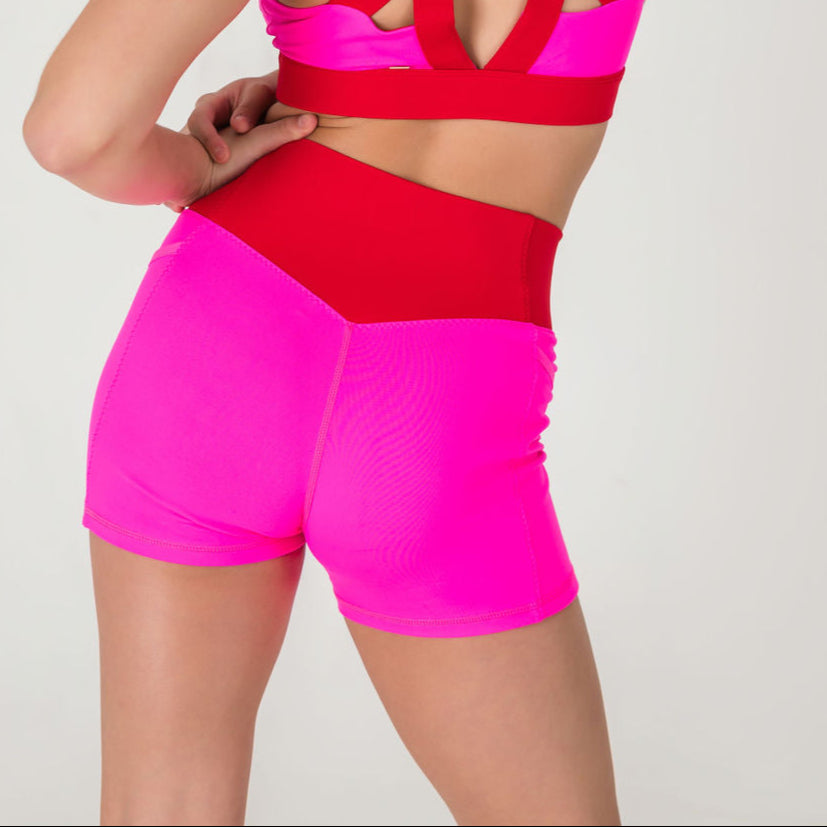 A person models the Chic Shorts - Punch Pink, featuring a trendy pink and red color-block design, shown from the waist down with one hand on their hip against a plain white background.