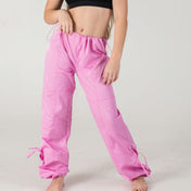 A person stands barefoot against a plain light background wearing WOW Parachute Pants in Sweet Pink and a black crop top. Their face is not visible.