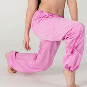 A person wearing WOW Parachute Pants in a loose fit pink style kneels on one knee against a plain light background, with only the pants visible as their upper body and face are not shown.