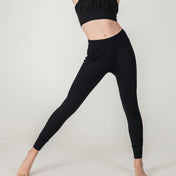 A person in a black crop top and XOXO Skinny Joggers - FINAL SALE stands with legs apart against a plain white background, showcasing modern athleisure. Their face is not shown.