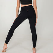 A person stands barefoot on a light background, wearing black XOXO Skinny Joggers and a matching crop top, with one leg straight and the other bent outward, hands on their thighs for an easy athleisure vibe.