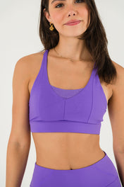 A woman in Bonbon Royal Purple Shorts and a matching sports bra stands against a plain white background, smiling slightly.