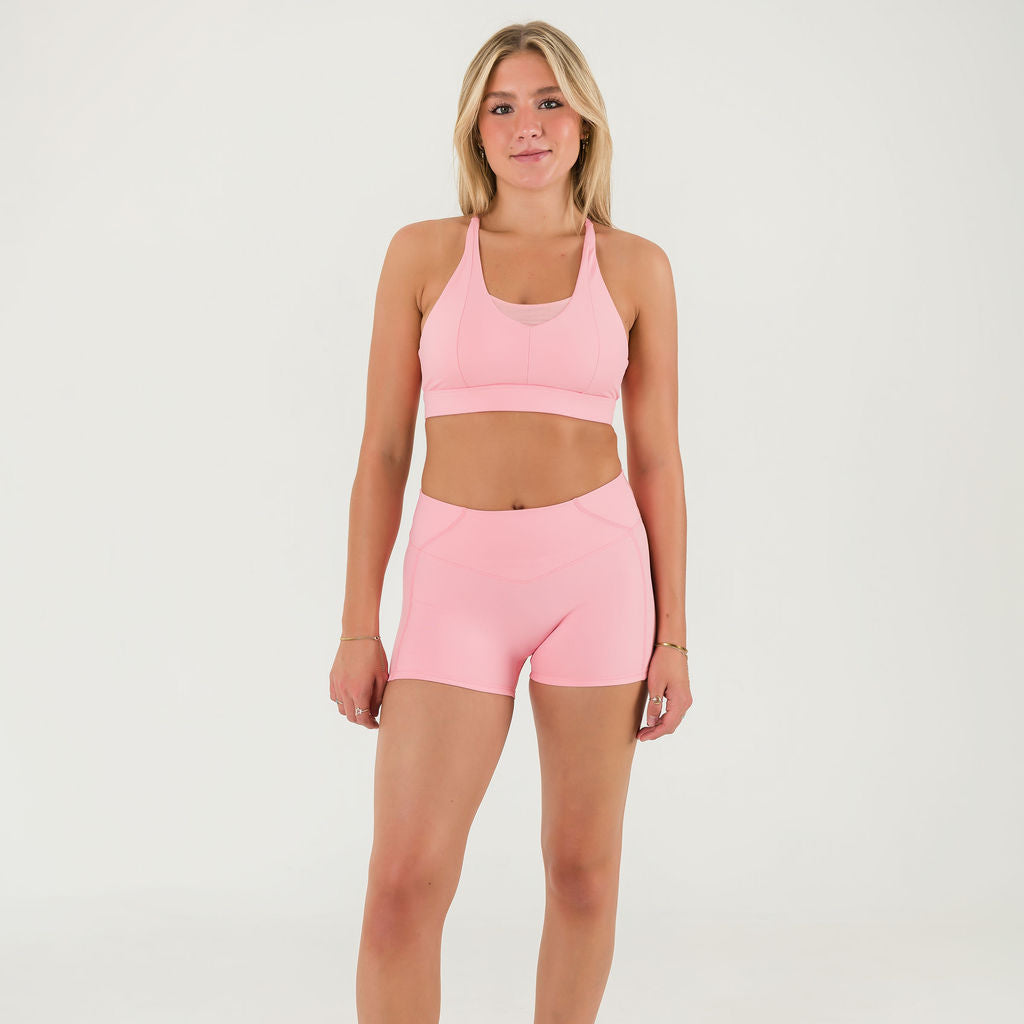 A woman stands against a plain white background, wearing the Bonbon Vivid Pink Top with a scoop neckline and matching high-waisted athletic shorts, her arms relaxed by her sides.