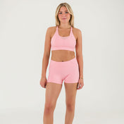 A woman stands against a plain white background, wearing the Bonbon Vivid Pink Top with a scoop neckline and matching high-waisted athletic shorts, her arms relaxed by her sides.