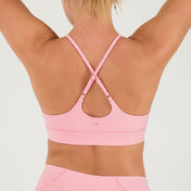 A woman with blonde hair in a ponytail wears the Bonbon Vivid Pink Top and matching leggings, raising her arms to showcase the top’s adjustable crisscross straps against a plain white background.