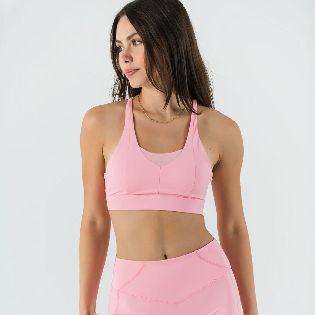 A woman stands against a white background, wearing the Bonbon Top in Vivid Pink featuring a mesh scoop neckline and matching high-waisted athletic shorts. She looks to the side with her arms relaxed at her sides.