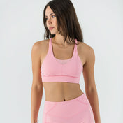A woman stands against a white background, wearing the Bonbon Top in Vivid Pink featuring a mesh scoop neckline and matching high-waisted athletic shorts. She looks to the side with her arms relaxed at her sides.