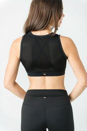 A woman with long brown hair stands with hands on hips, back facing the camera, wearing the WOW Mesh Top in black with built-in bra and high-waisted leggings—perfect for any dance wardrobe—against a plain light background.