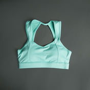 The Allure Mint Top, a light turquoise sports bra with racerback straps and contrast stitching, is displayed flat on a dark gray background.