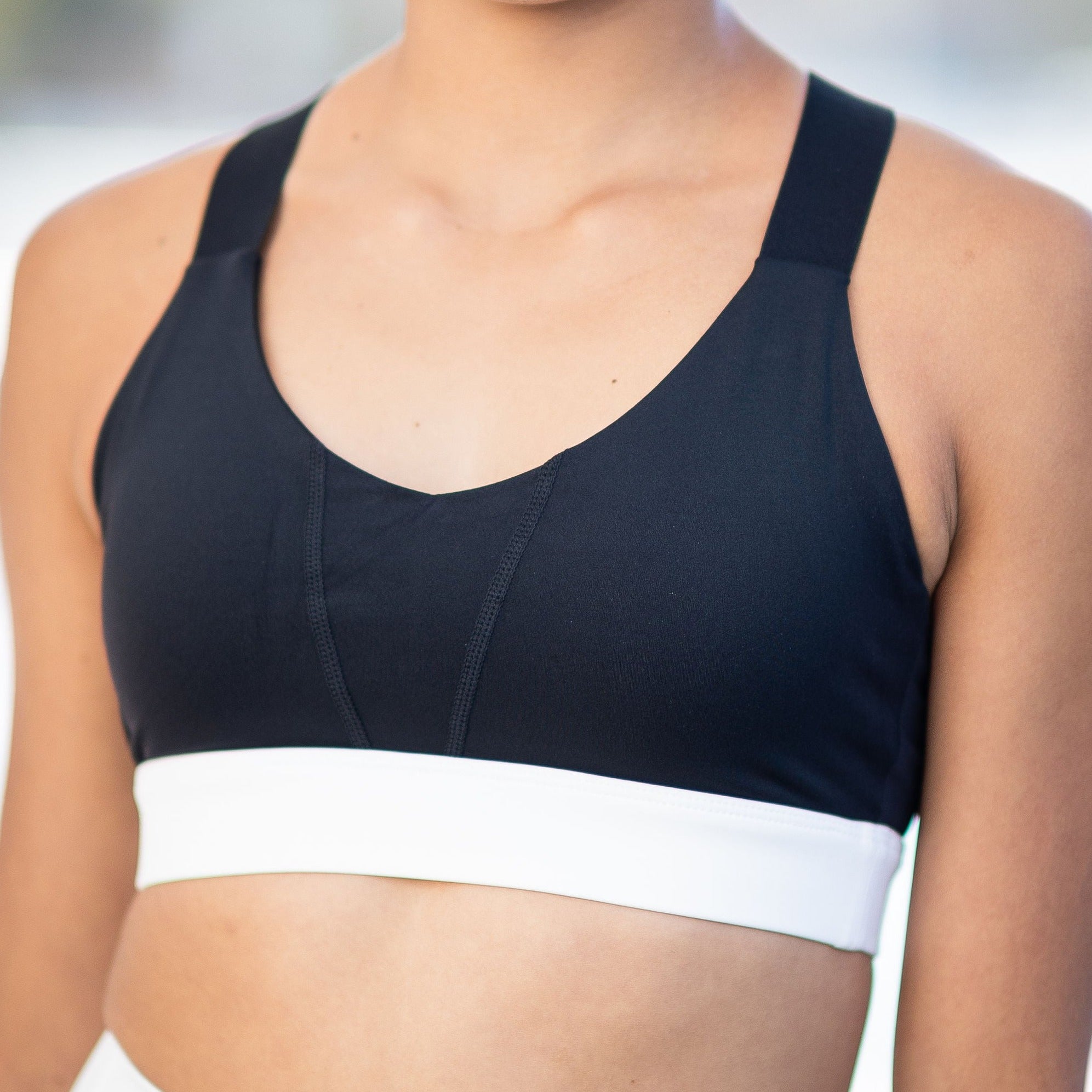 Someone is wearing the Chic Top - Charcoal, featuring a black and white design with wide straps and a white band under the bust. The photo displays their upper torso and shoulders, but their face is not shown.